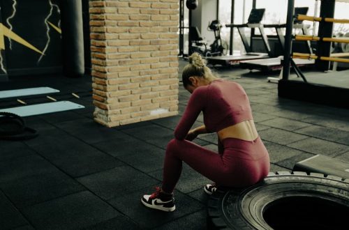 A woman in sportswear rests on a tire during gym training, showcasing fitness dedication.