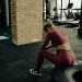 A woman in sportswear rests on a tire during gym training, showcasing fitness dedication.
